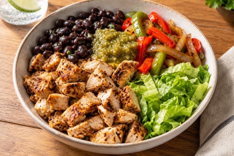 A bowl of grilled chicken, black beans, fajita peppers and onions, tomatillo green salsa and chopped romaine with no rice