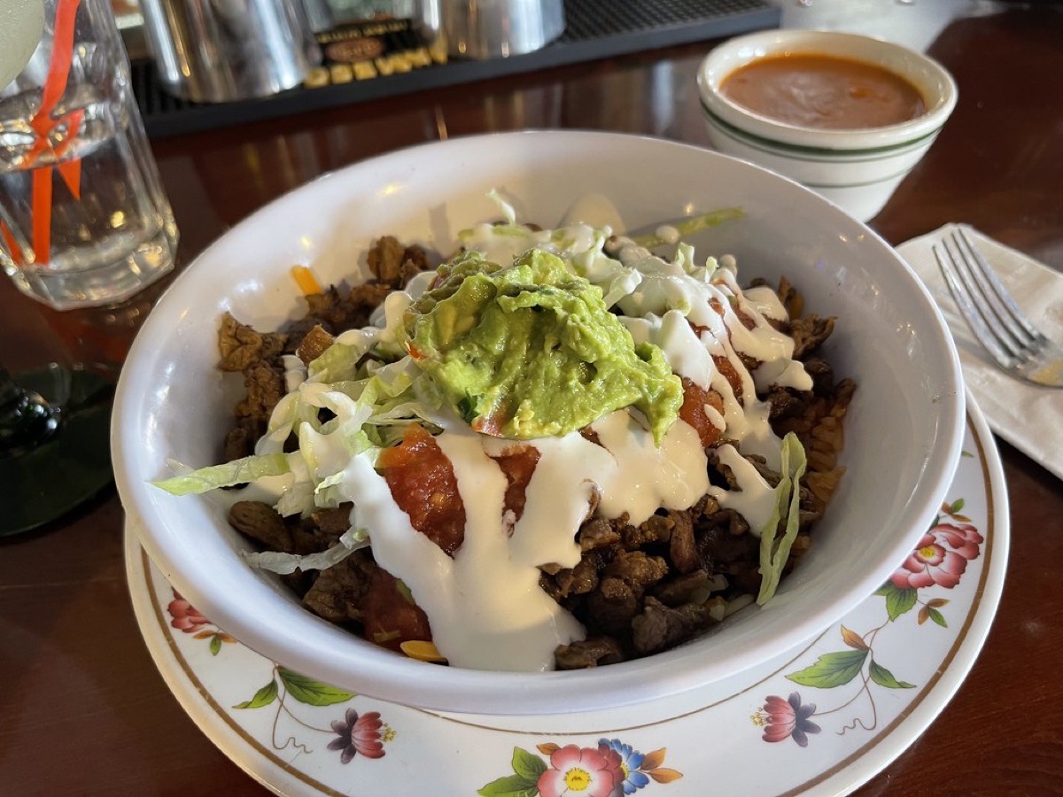 A burrito bowl topped with guacamole, sour cream, salsa and lettuce